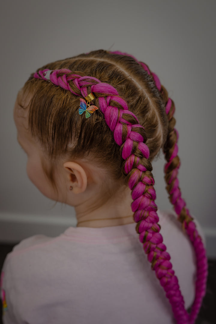 Close-up of a pink braid with a butterfly charm, styled by Braids by Kandy using Aunty Cherish hair.